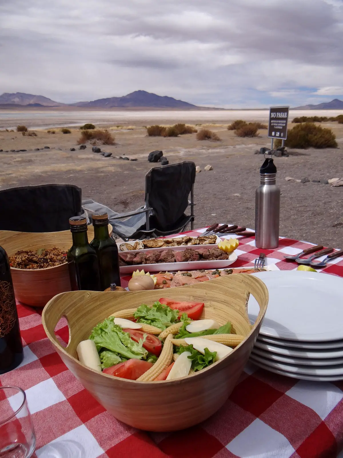 Picture of table with salad on the foreground and other meat dishes, set in front of a salt flat in the Atacama Desert