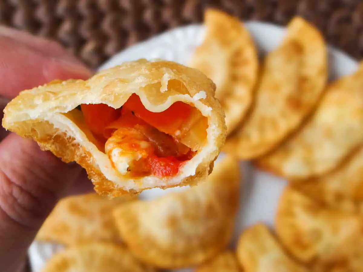 Image of cross section cut of shrimp pastel showing its content: shrimp and tomatoes in a puffed fried dough pocket.